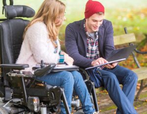 Woman in wheelchair looking at book with man in beanie